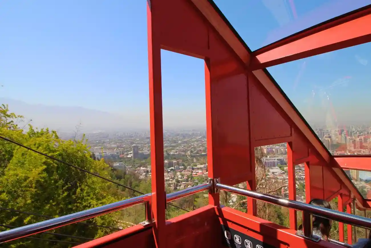 Vista panorámica de Santiago desde el interior del carro rojo del Funicular, enmarcada por la estructura metálica